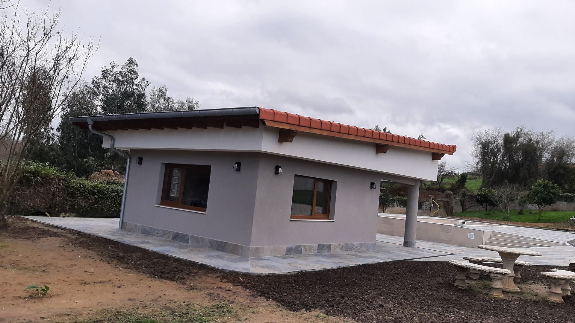 Una pequeña casa con techo de tejas rojas está situada en medio de un campo.