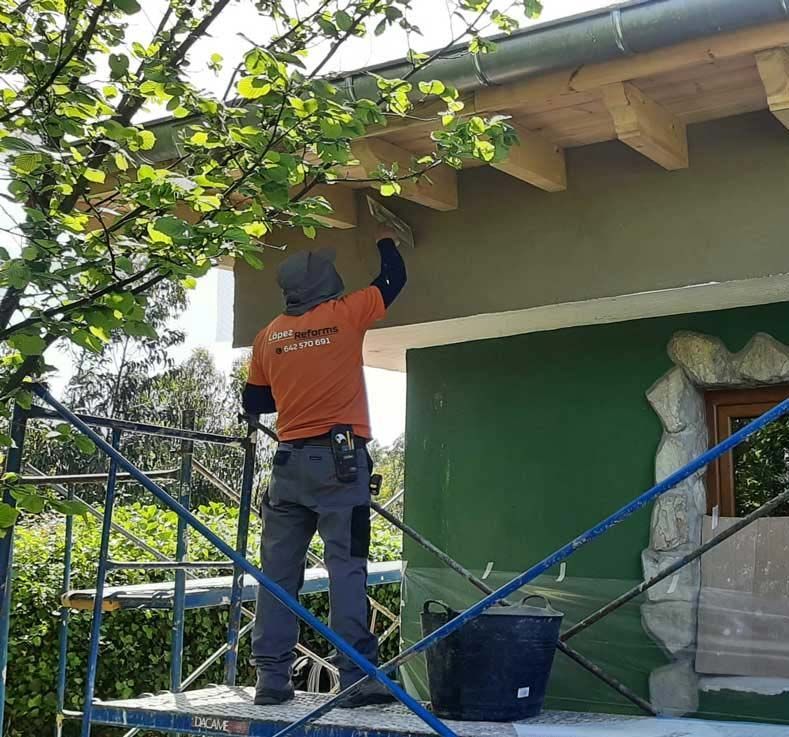 Un hombre está de pie sobre un andamio pintando un edificio verde.