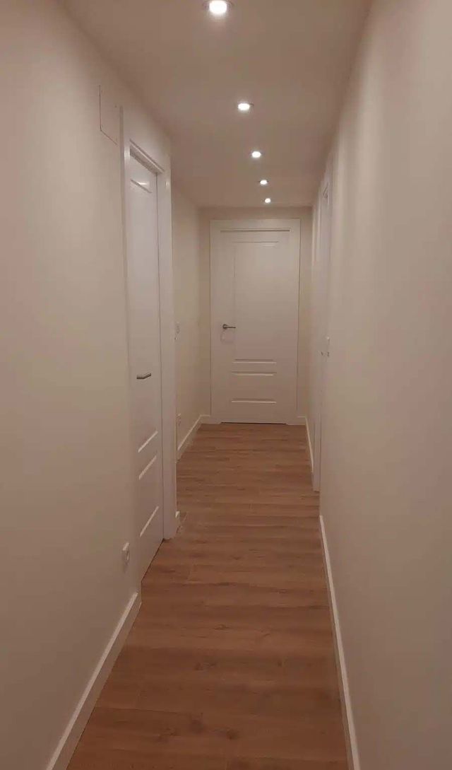 Un largo pasillo con suelos de madera y paredes blancas.