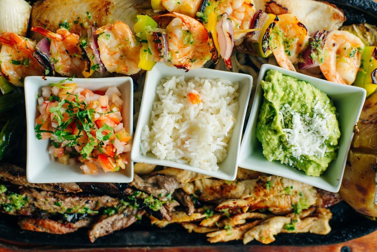 Un plato de comida con arroz, guacamole y camarones en una mesa.
