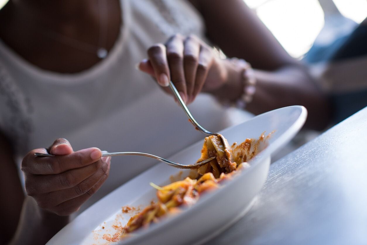 Una mujer está comiendo espaguetis con un tenedor de un plato blanco.