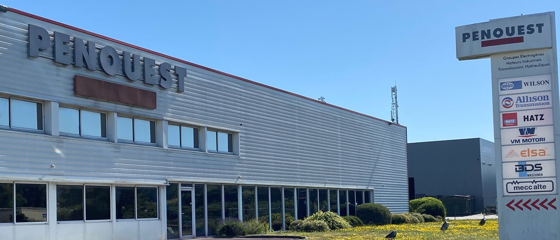 Extérieur du bâtiment PENOUEST avec des panneaux listant les services et marques distribuées.