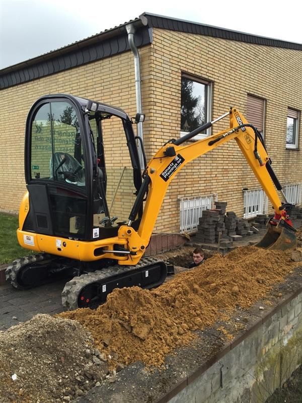 Ein gelber Bagger gräbt ein Loch vor einem Backsteingebäude