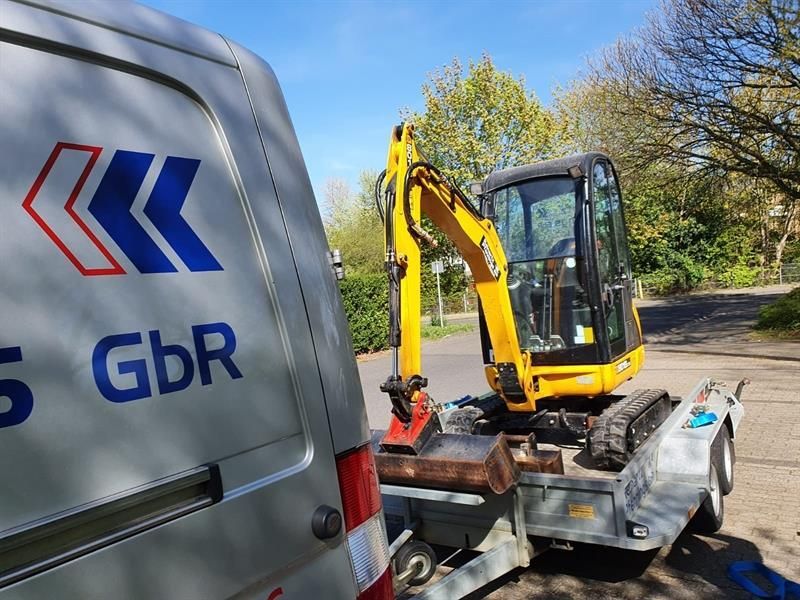 Ein kleiner Bagger auf einem Anhänger neben einem Lieferwagen mit der Aufschrift „GBR“