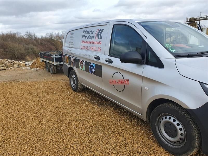 Ein weißer Lieferwagen parkt auf einer Schotterstraße.