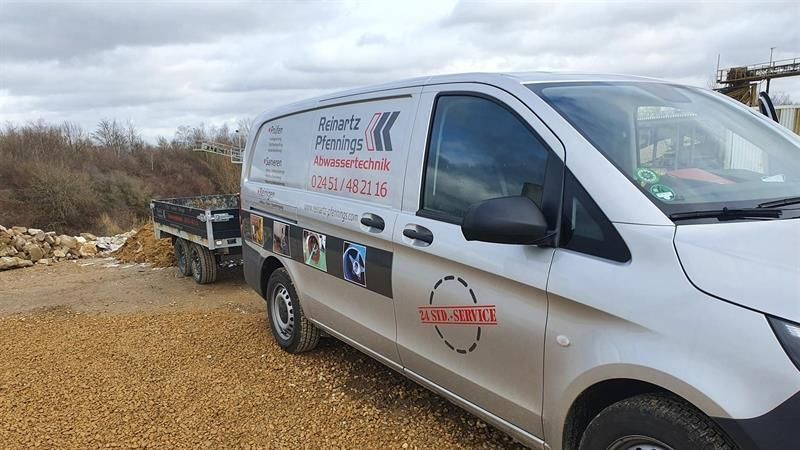 Ein weißer Lieferwagen parkt neben einem Anhänger auf einer Schotterstraße.