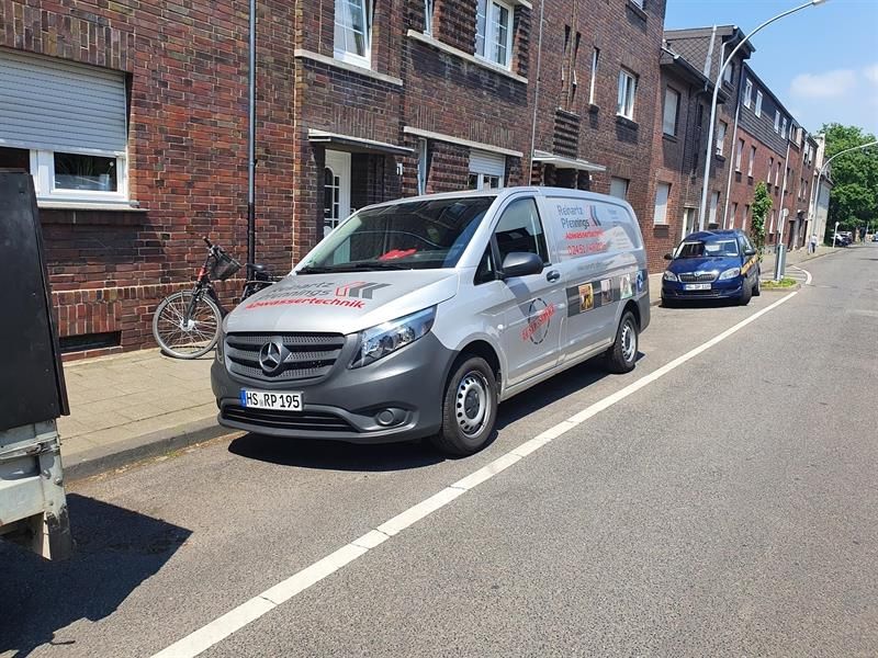 Ein Lieferwagen steht am Straßenrand vor einem Backsteingebäude.