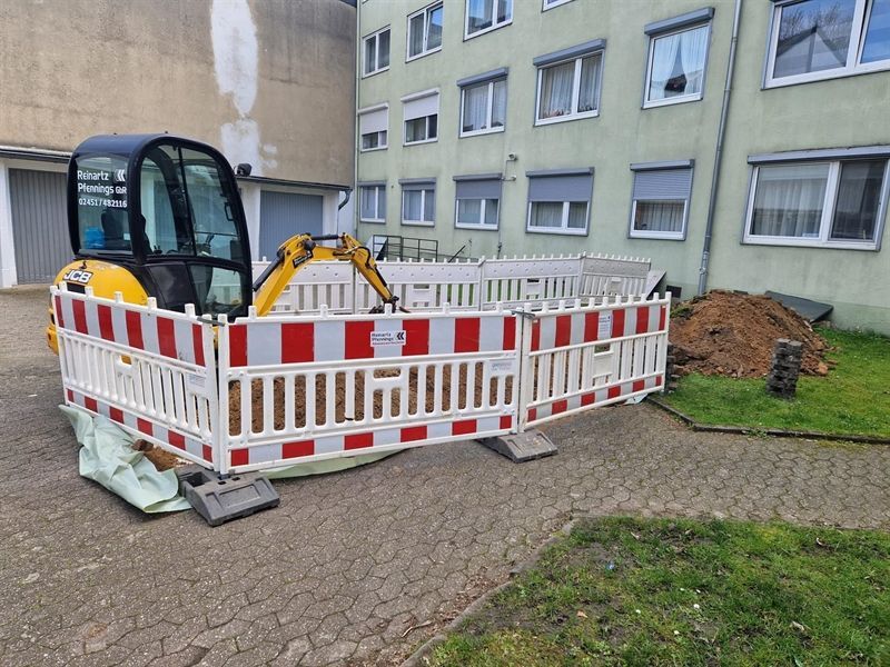 Ein gelb-schwarzer Bagger steht auf einem eingezäunten Gelände vor einem Gebäude.