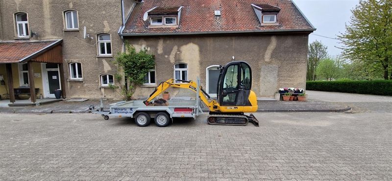 Ein kleiner gelber Bagger steht auf einem Anhänger vor einem Haus.