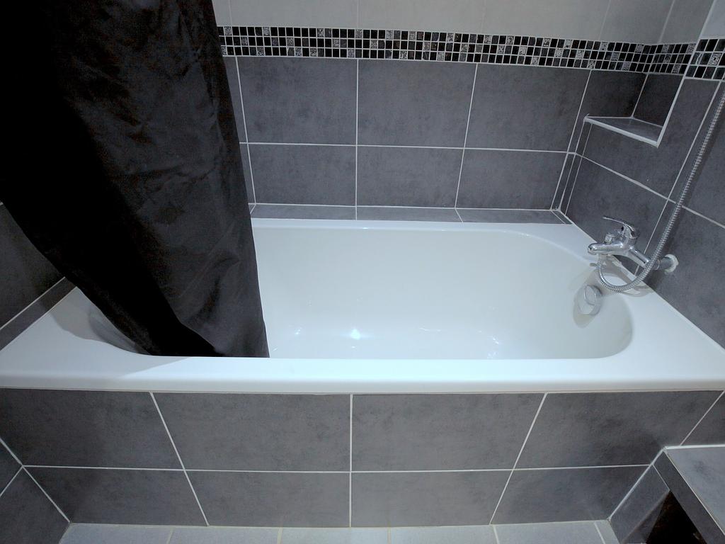 Baignoire blanche entourée de carrelage gris et rideau de douche noir - réalisations