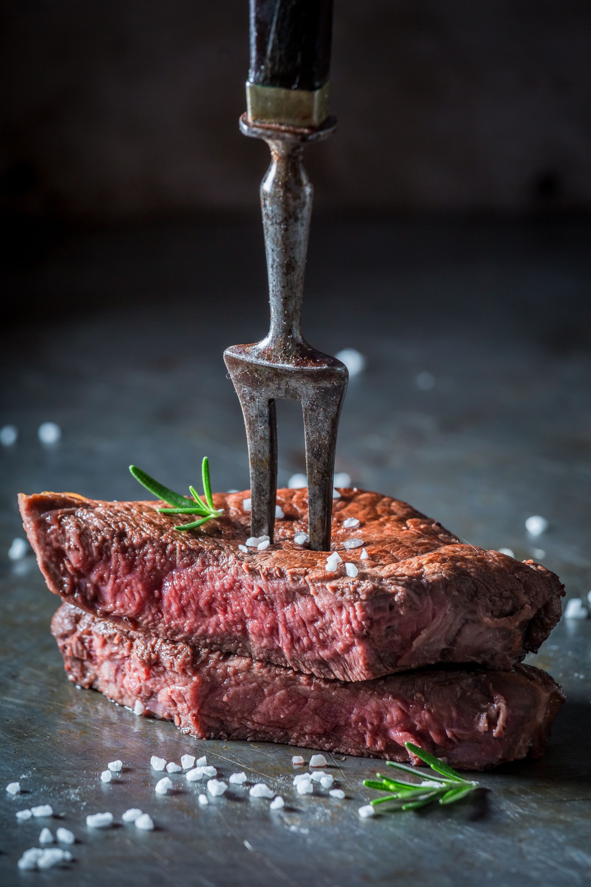 In Scheiben geschnittenes Steak, mit einer Gabel aufgespießt, garniert mit Rosmarin und Salz.
