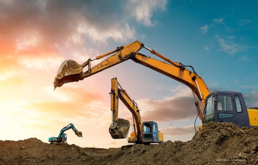 Bagger heben bei Sonnenuntergang auf einer Baustelle einen Erdhügel aus.