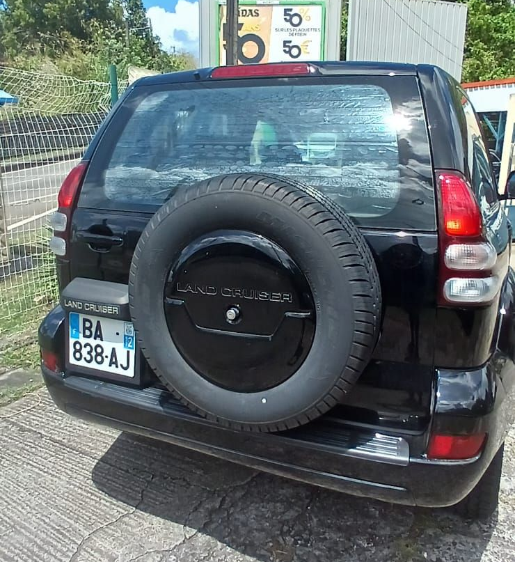 Un Toyota Land Cruiser noir vu de l'arrière, avec une roue de secours montée sur le hayon et des plaques d'immatriculation françaises.