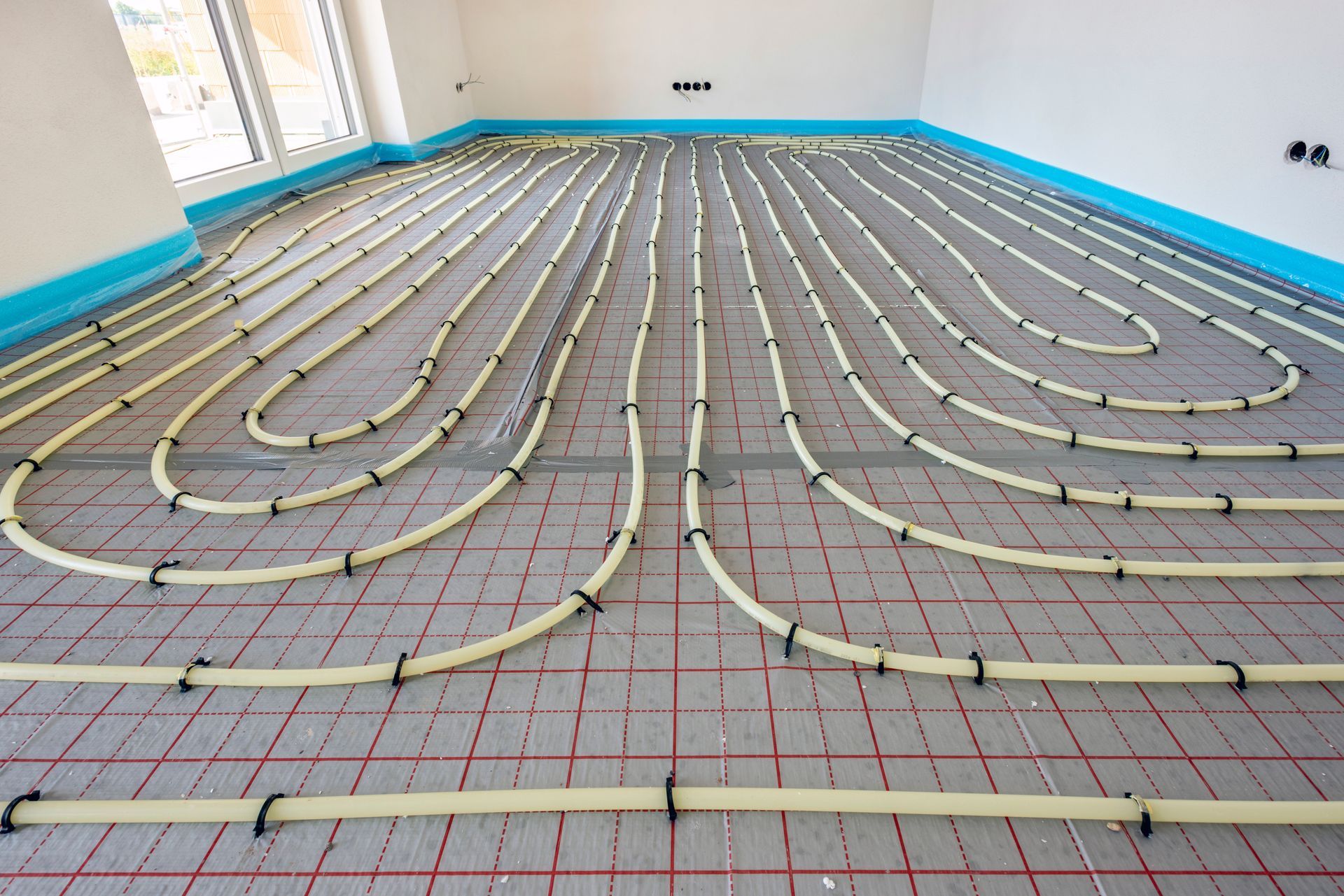 Tuyauterie pour chauffage au sol radiant installée sur une dalle de béton avec des lignes de quadrillage rouges et une isolation périphérique bleue.
