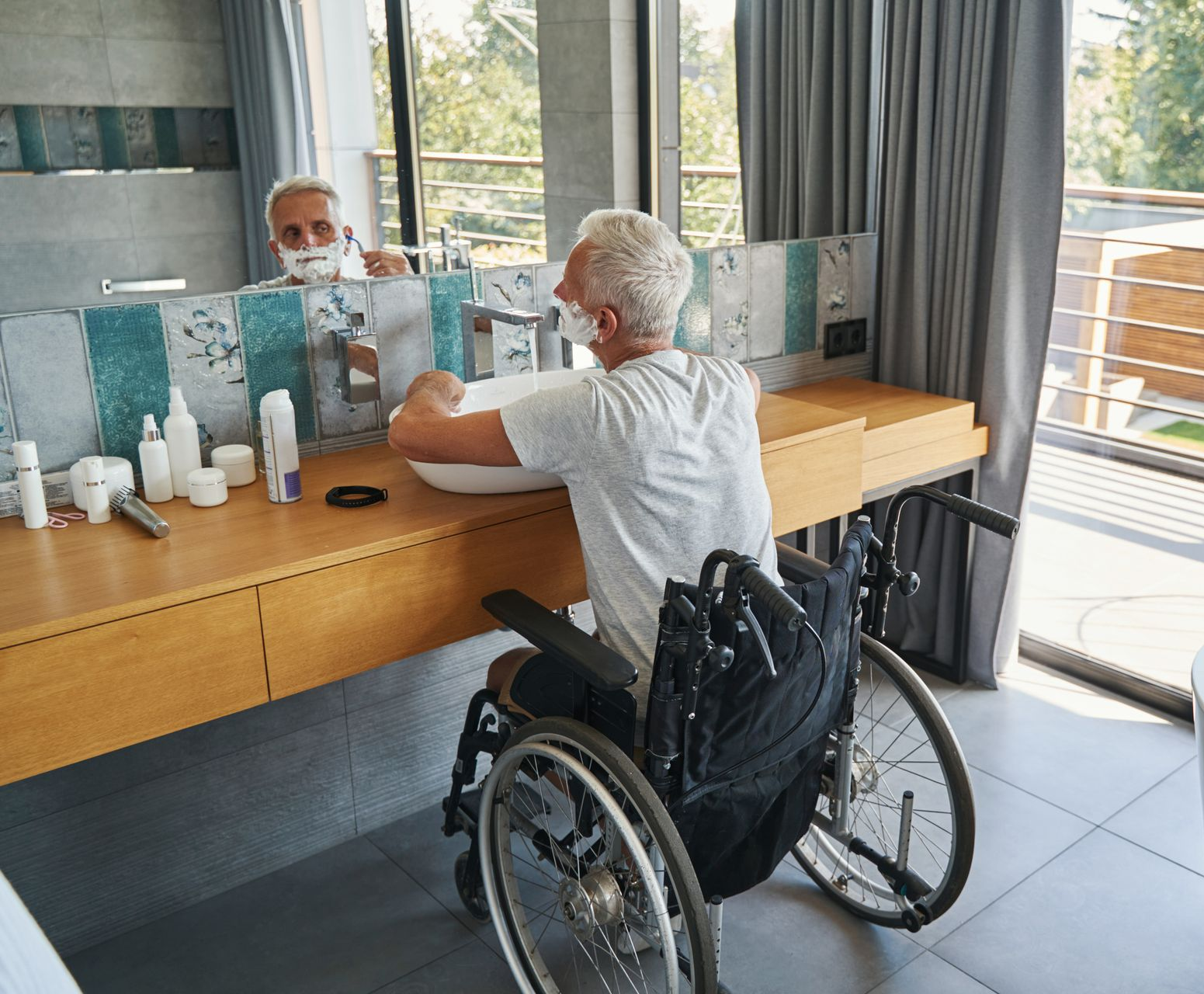 Un homme en fauteuil roulant qui se rase dans une salle de bains PMR.