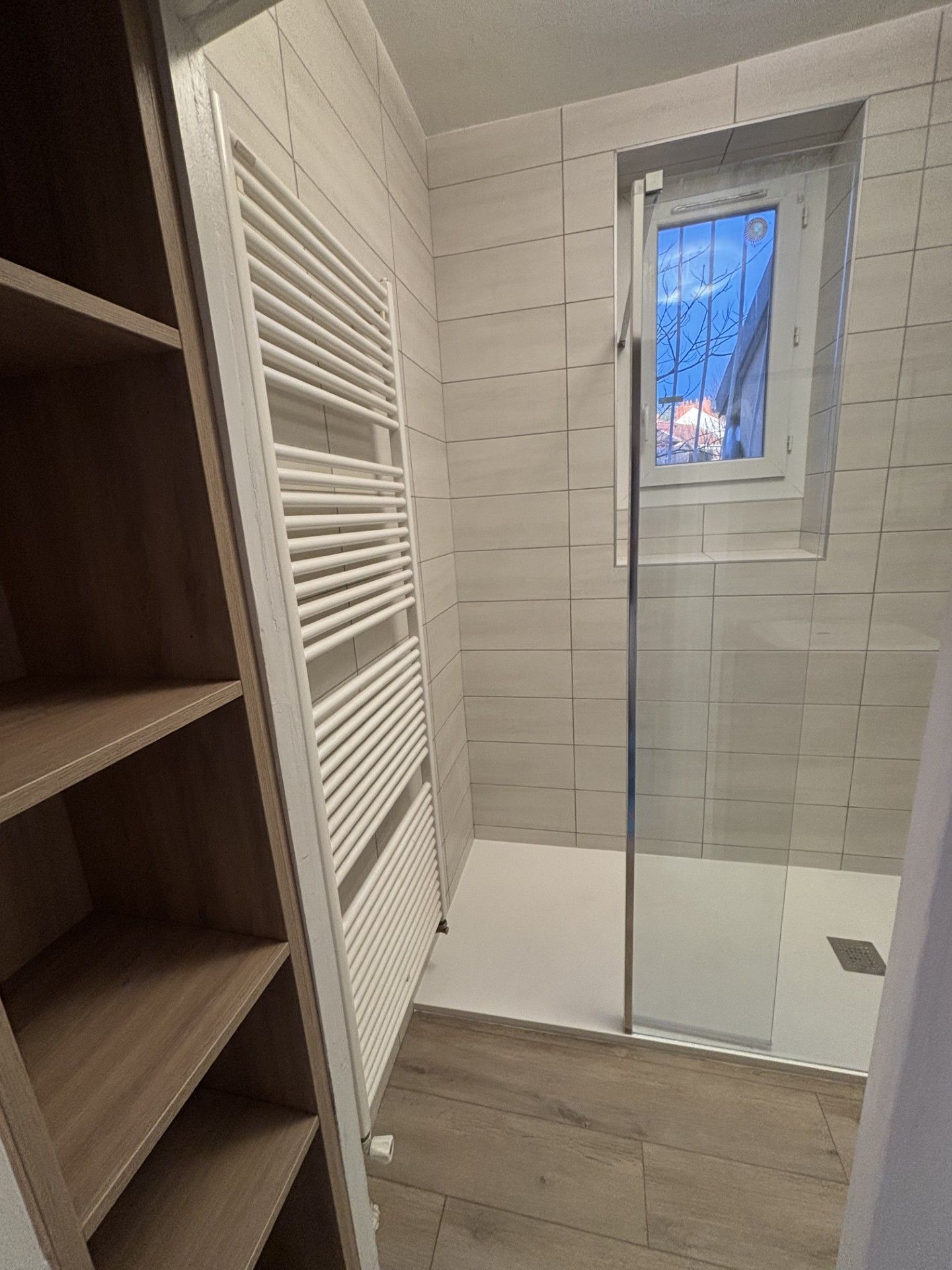 Un douche à l'italienne avec un sèche-serviette et une étagère.