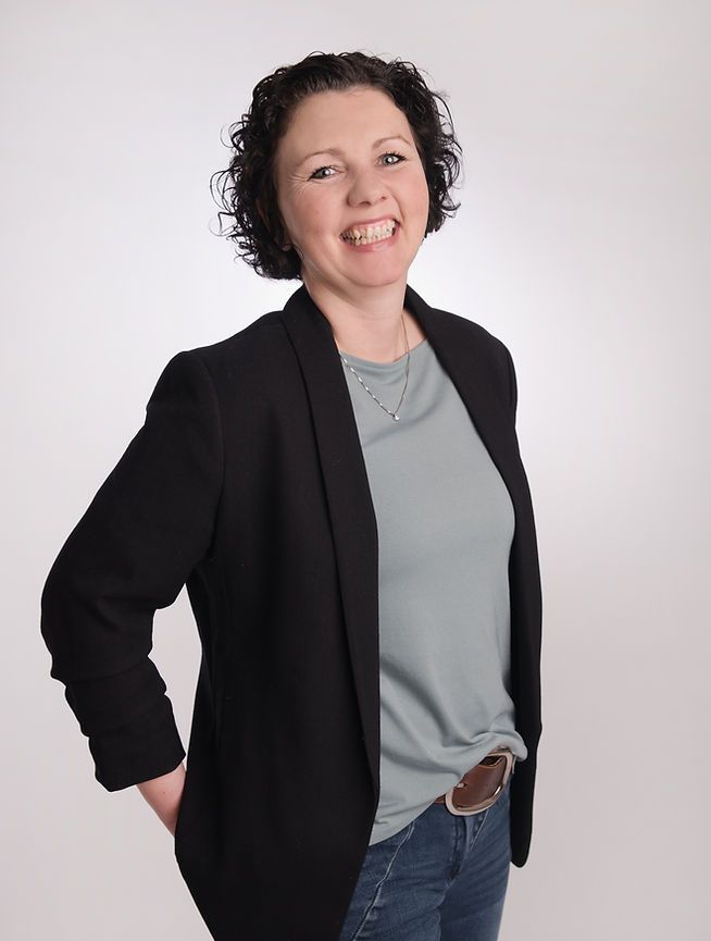 Eine Frau in einer schwarzen Jacke und einem grauen Hemd lächelt.