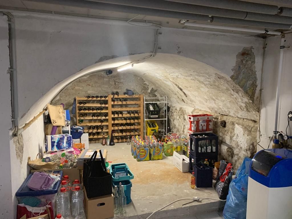 Lagerraum mit gewölbter Decke, Regalen und verschiedenen Gegenständen. Weiße Wände und Betonboden.