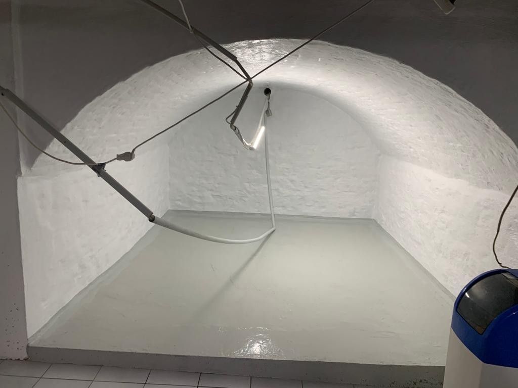 Innenansicht eines gewölbten, weiß gestrichenen Raums mit hellgrauem Boden. Über der Decke befinden sich Beleuchtungskörper.