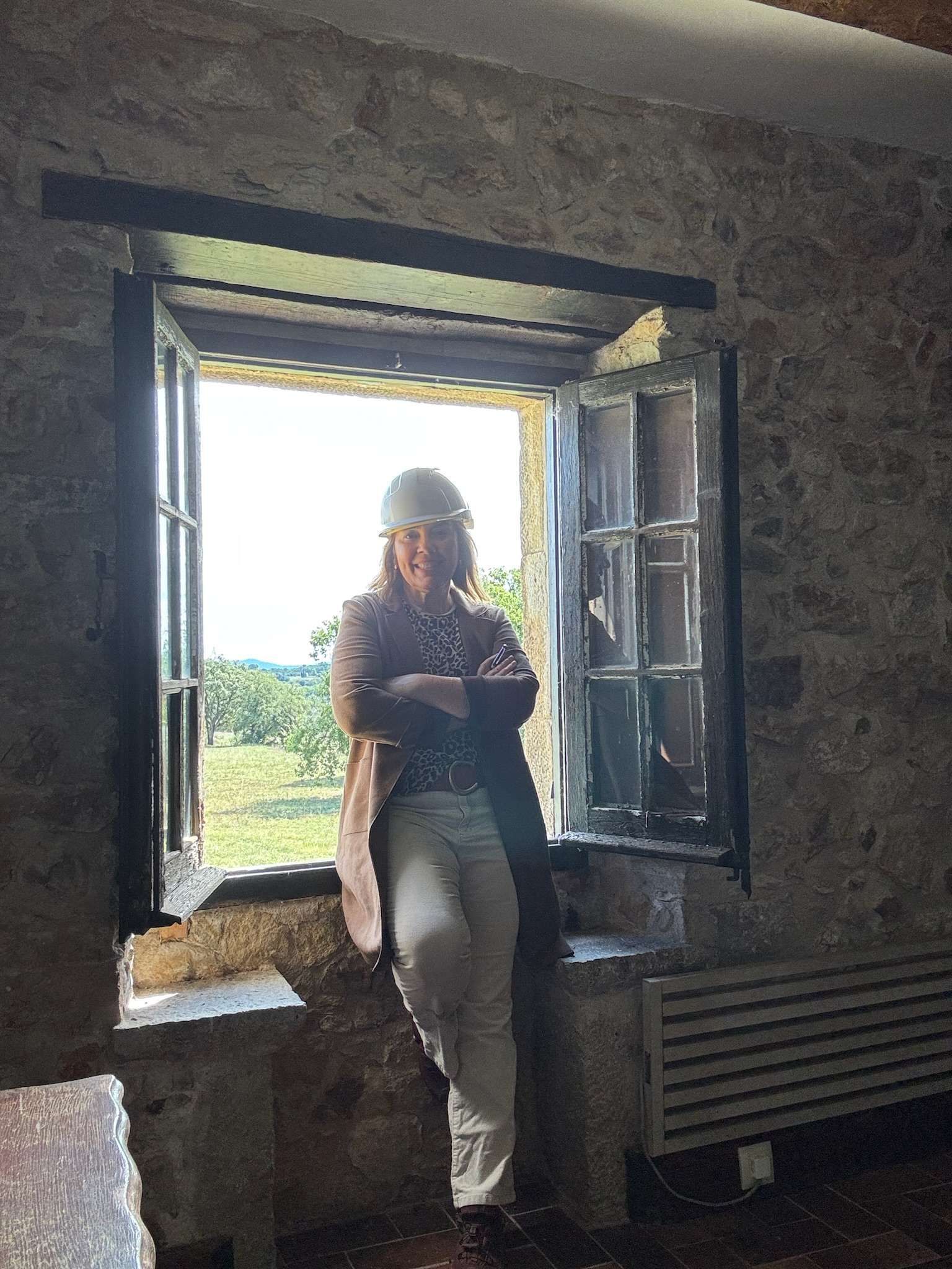 Mujer en la ventana con los brazos cruzados, con chaqueta, mirando el paisaje.