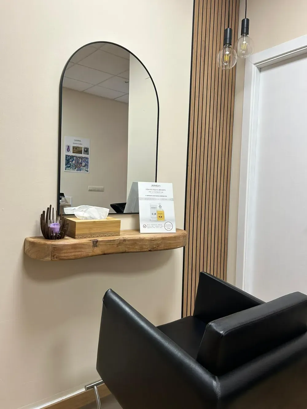 Un espacio de peluquería con un espejo arqueado sobre una repisa de madera con borde natural.