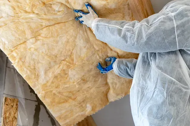 Persona instalando aislamiento amarillo, con guantes y traje de protección.