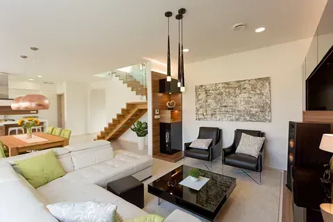 Sala de estar de concepto abierto con sofá seccional beige, escaleras, comedor, arte moderno y muebles con detalles en negro.