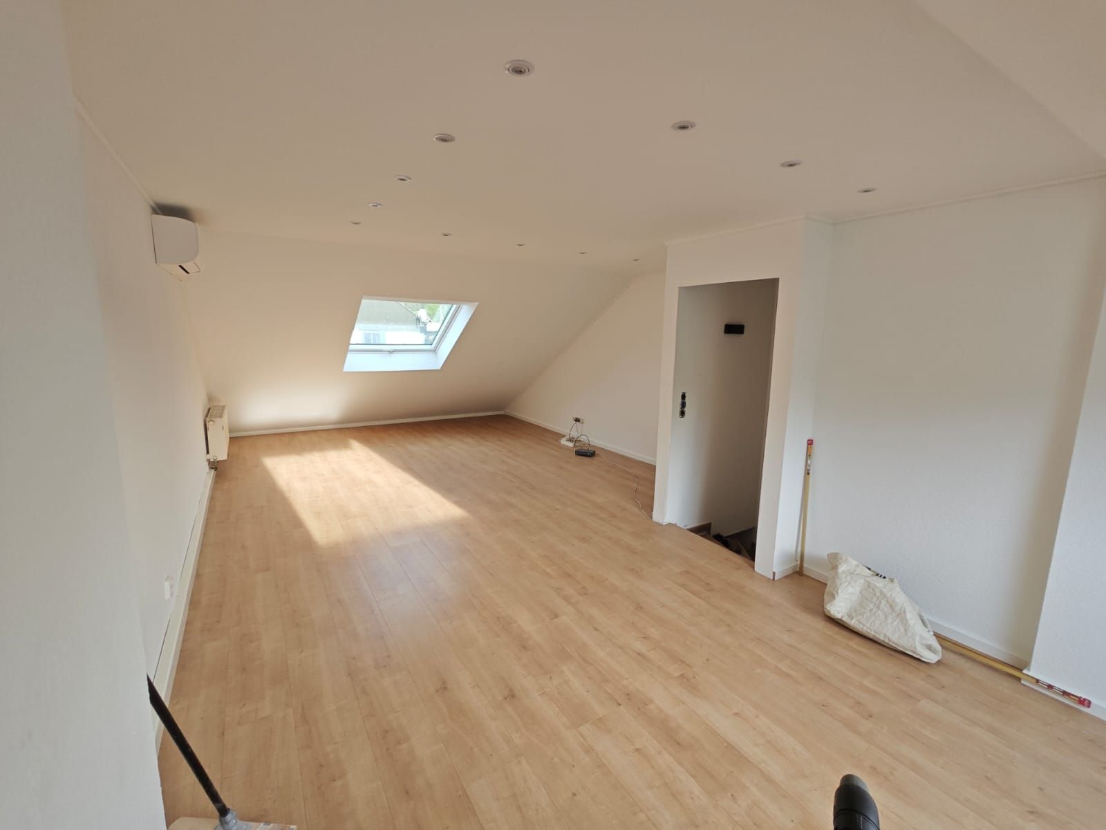 Leeres Zimmer mit Dachschräge, Oberlicht und Holzbodenoptik. Weiße Wände und Einbaustrahler.