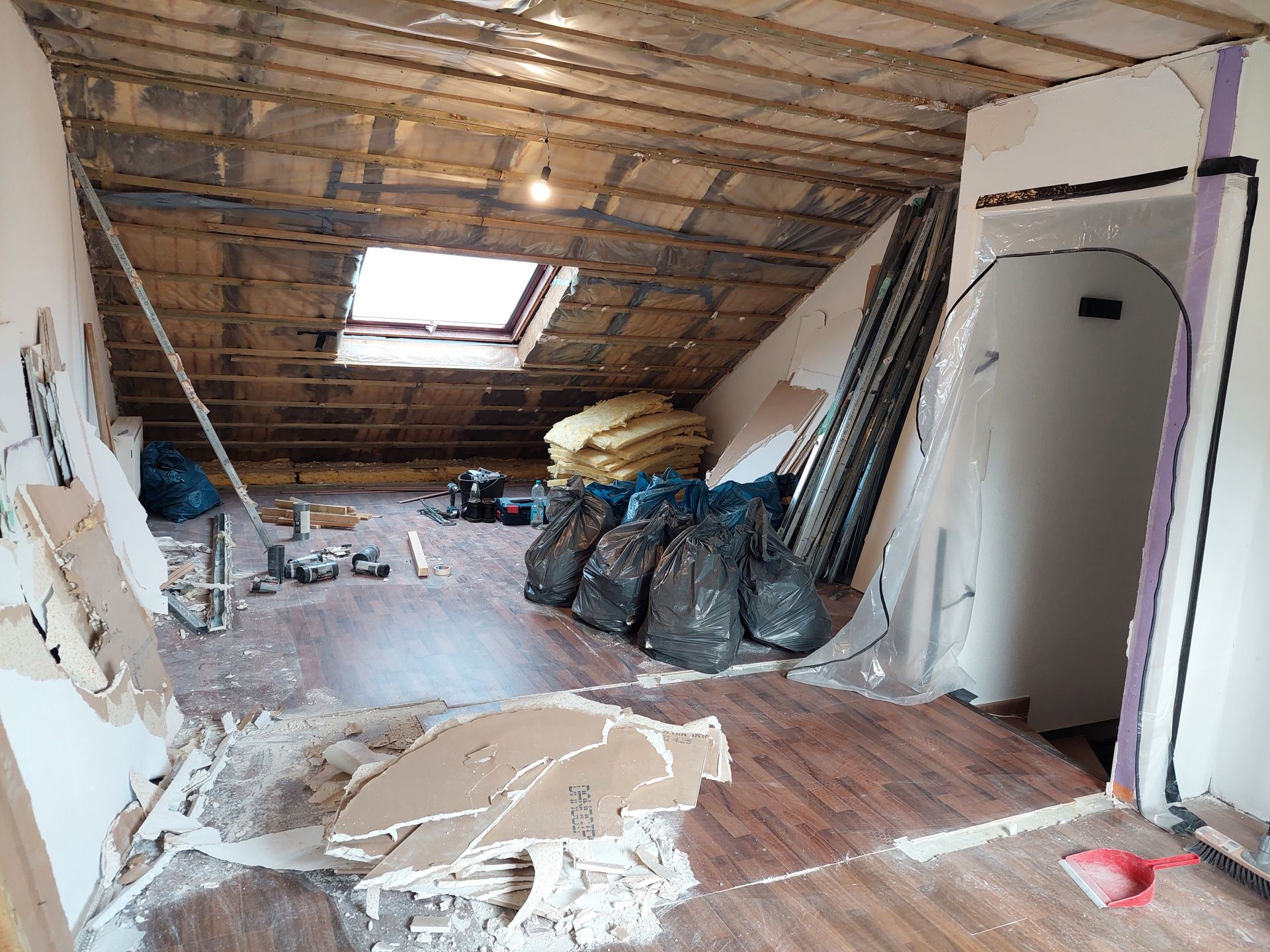 Der Dachboden wird renoviert. Freiliegende Balken, Dämmmaterial, Bauschutt und Werkzeuge liegen verstreut auf dem Boden. 