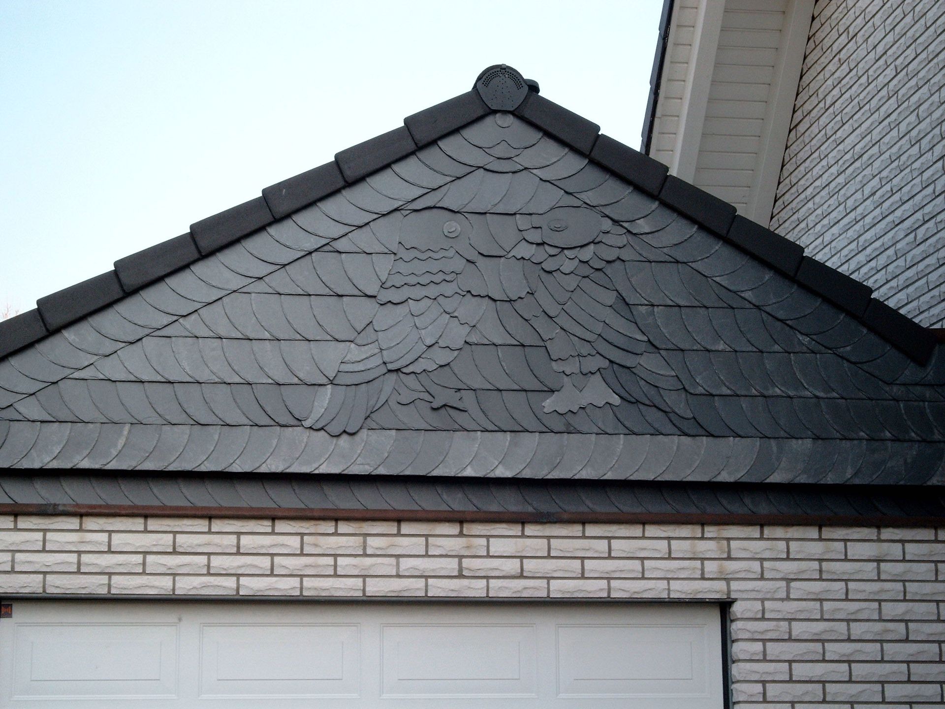 Schiefergedeckter Giebel mit Adlermotiv über einem Garagentor an einem Backsteingebäude.