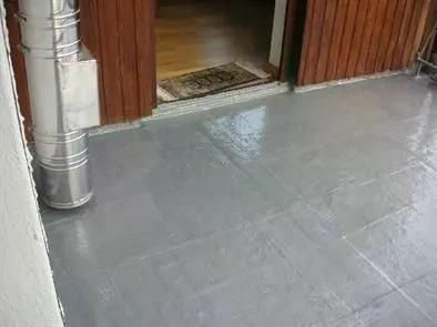 Eine grau gestrichene Betonveranda, eine Tür zum Innenraum und ein metallenes Schornsteinrohr.