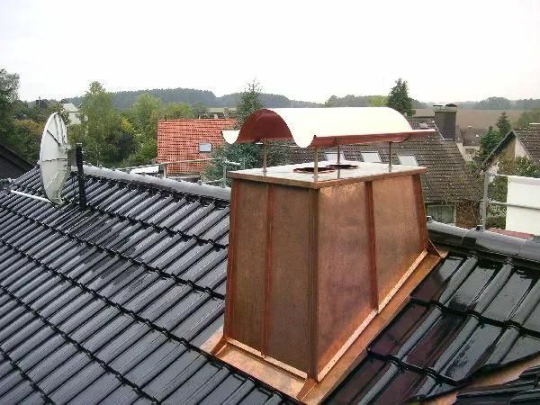 Kupferverkleideter Schornstein auf einem Ziegeldach mit gebogener Regenkappe aus Metall und Satellitenschüssel.