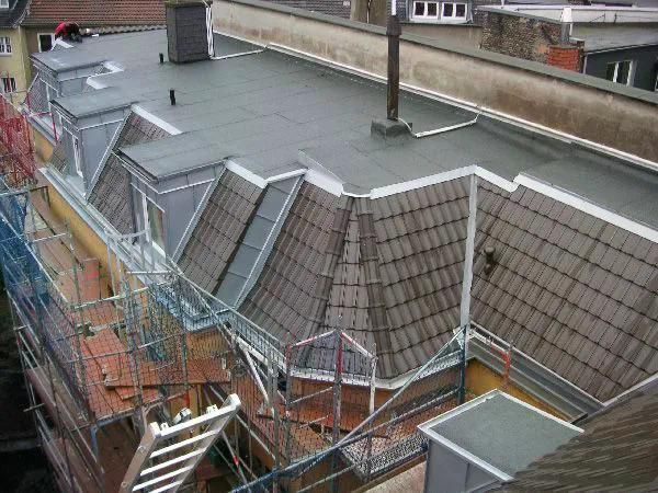 Dach mit Dachgauben, Ziegeldeckung und flachen Abschnitten; Gerüst an der Seite.