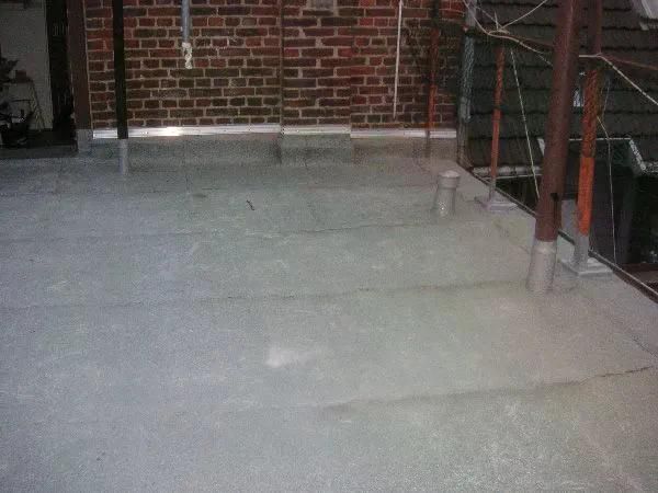 Betondach mit Backsteinmauer im Hintergrund und Metallstützen.