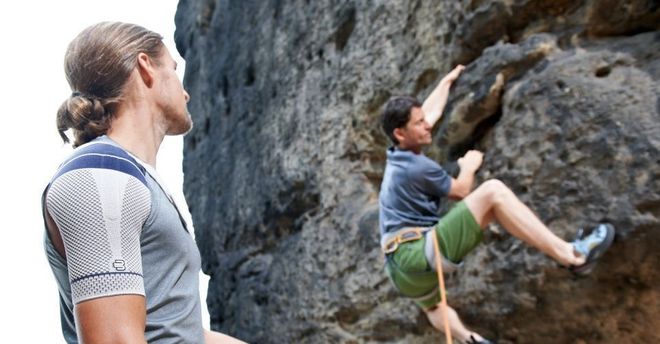 Ein Mann beobachtet einen anderen Mann beim Klettern auf einen Felsen.