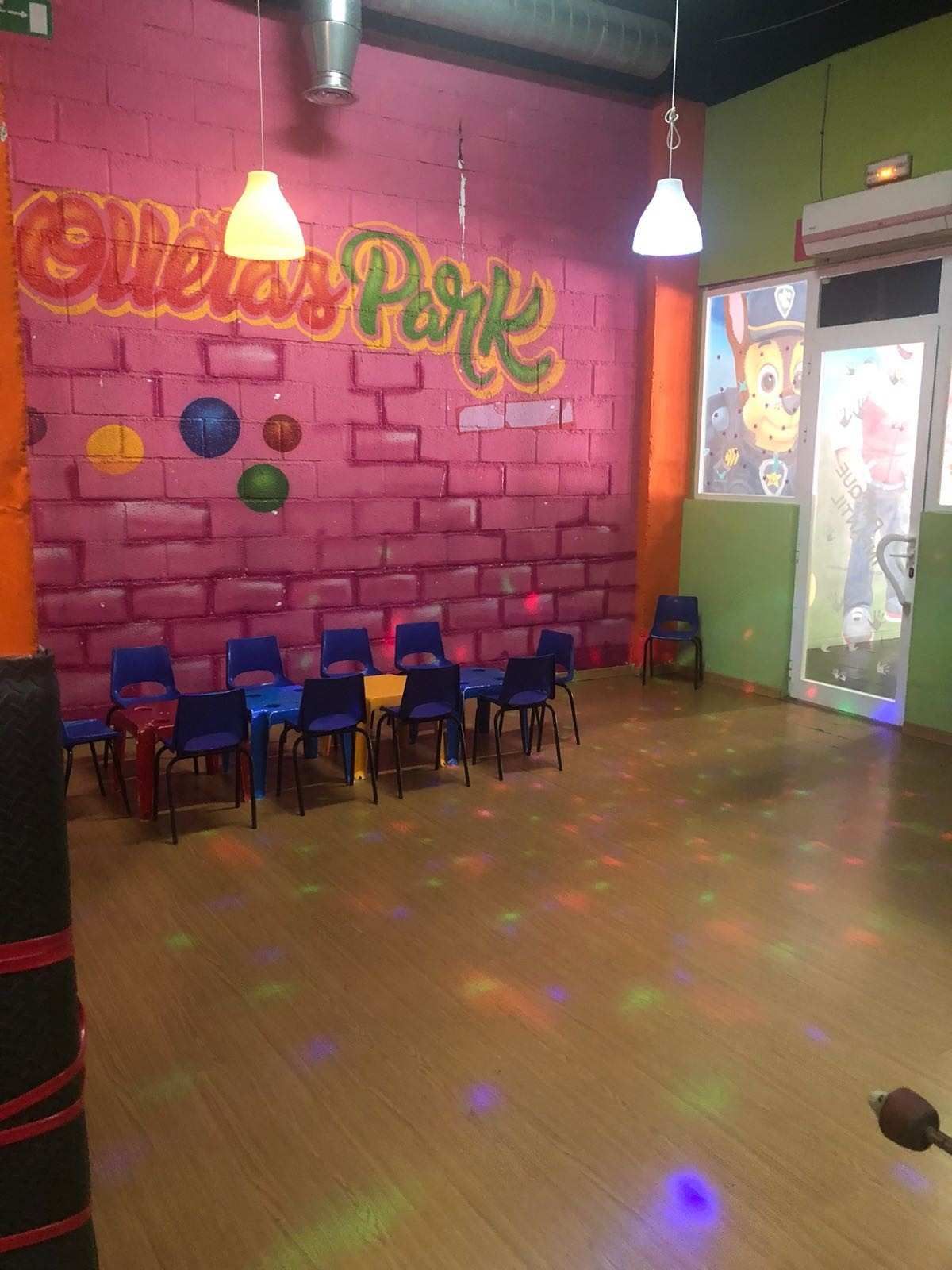 Local interior vacío con pared de ladrillo rosa, letrero de neón, sillas y reflejos de luz de colores en el suelo.