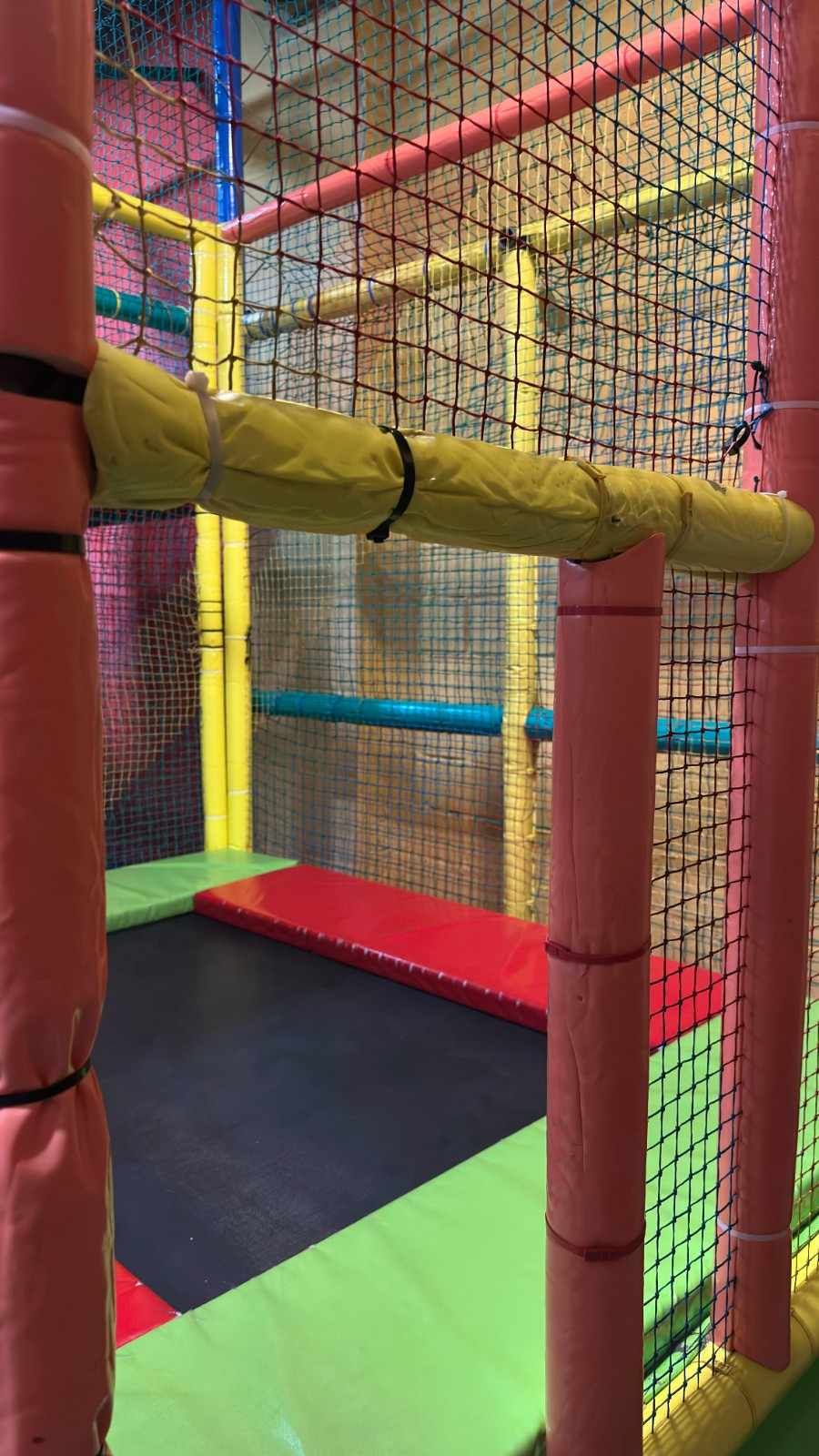 Zona de juegos interior colorida con estructuras blandas, túneles de malla acolchada y rampas para escalar.