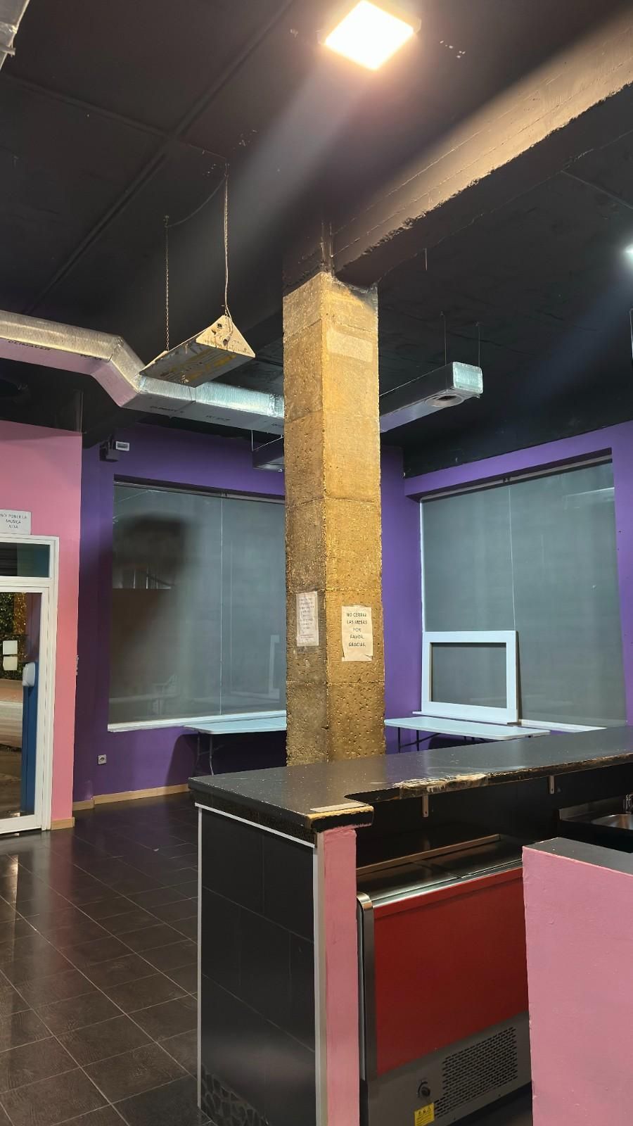 Interior vacío con paredes moradas, techo oscuro, pilar central y un mostrador negro en primer plano.