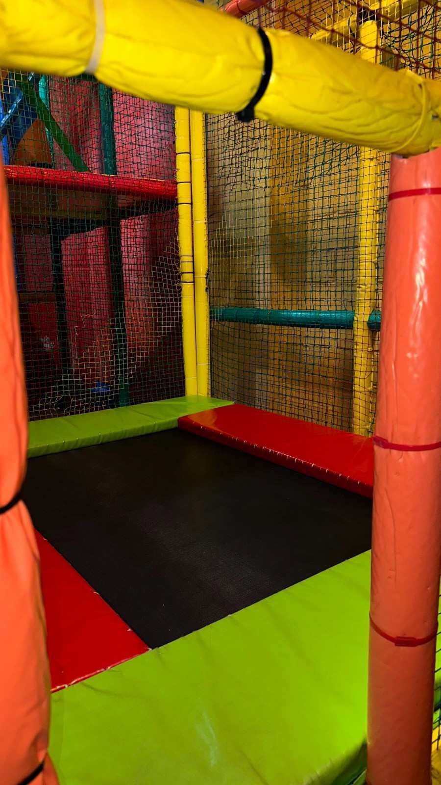 Túnel de juegos interior colorido con paredes acolchadas, red y suelo negro y verde.