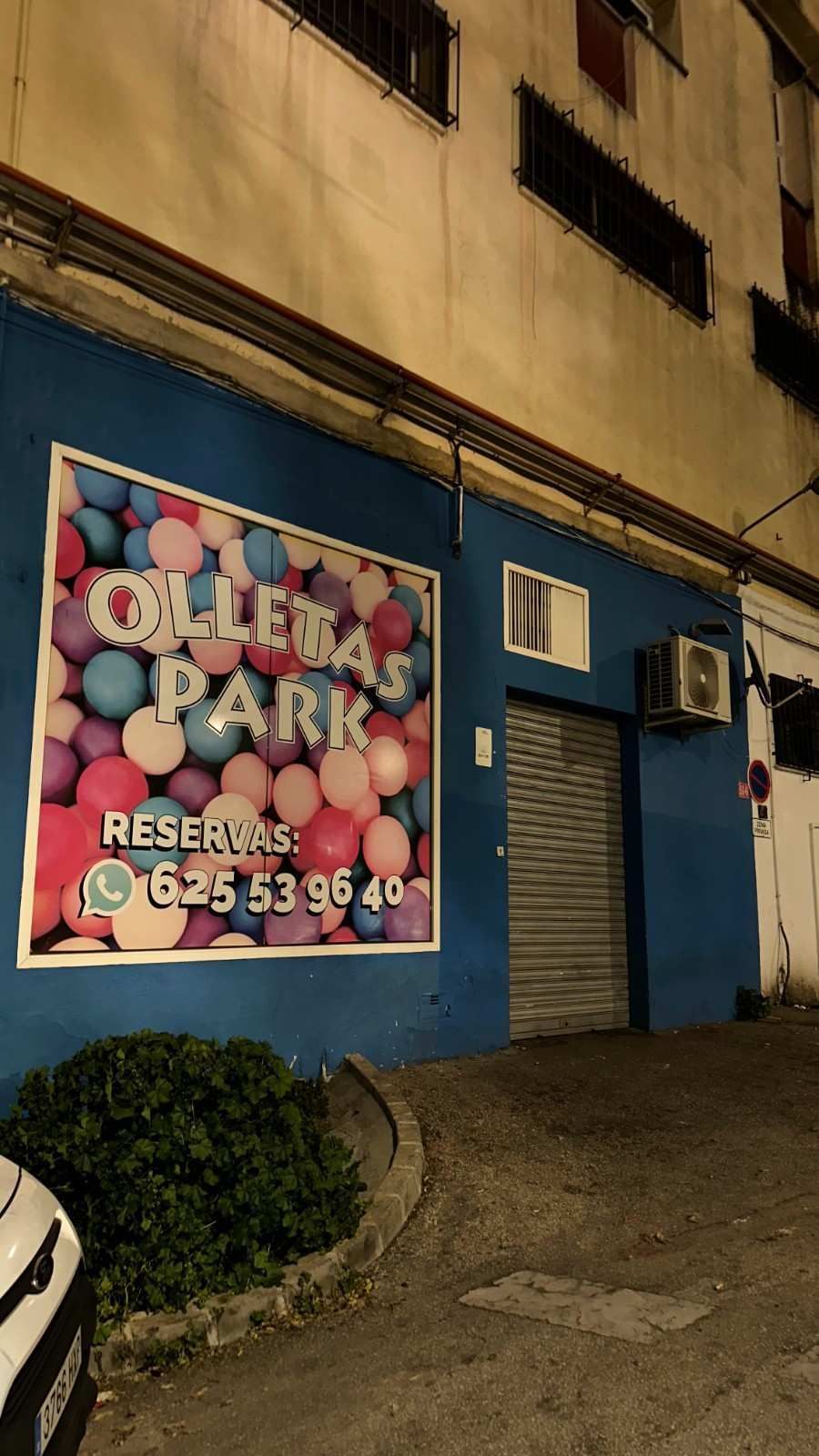 Fachada azul con un letrero rosa de “Cola Park” y una puerta cerrada por la noche.