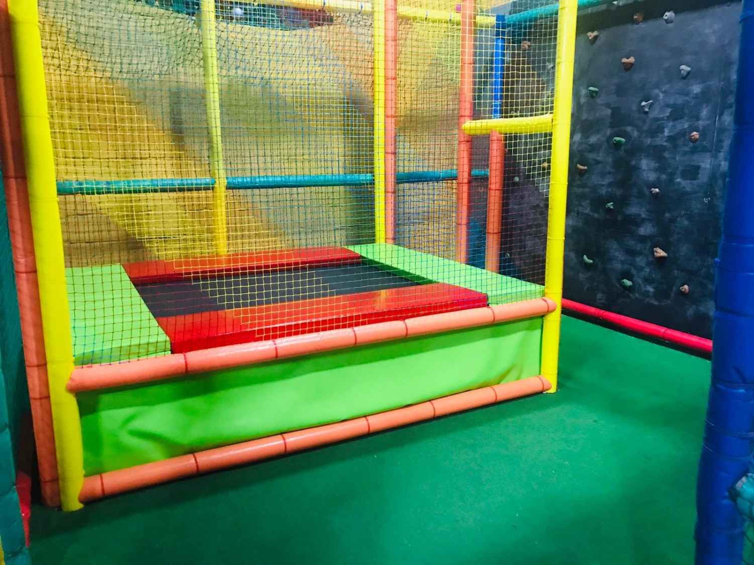 Zona de juegos interior colorida con cama elástica con red y suelo acolchado de espuma.