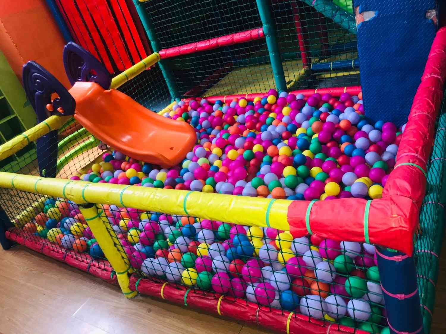 Piscina de bolas interior con un pequeño tobogán naranja y una colorida red de seguridad de espuma.