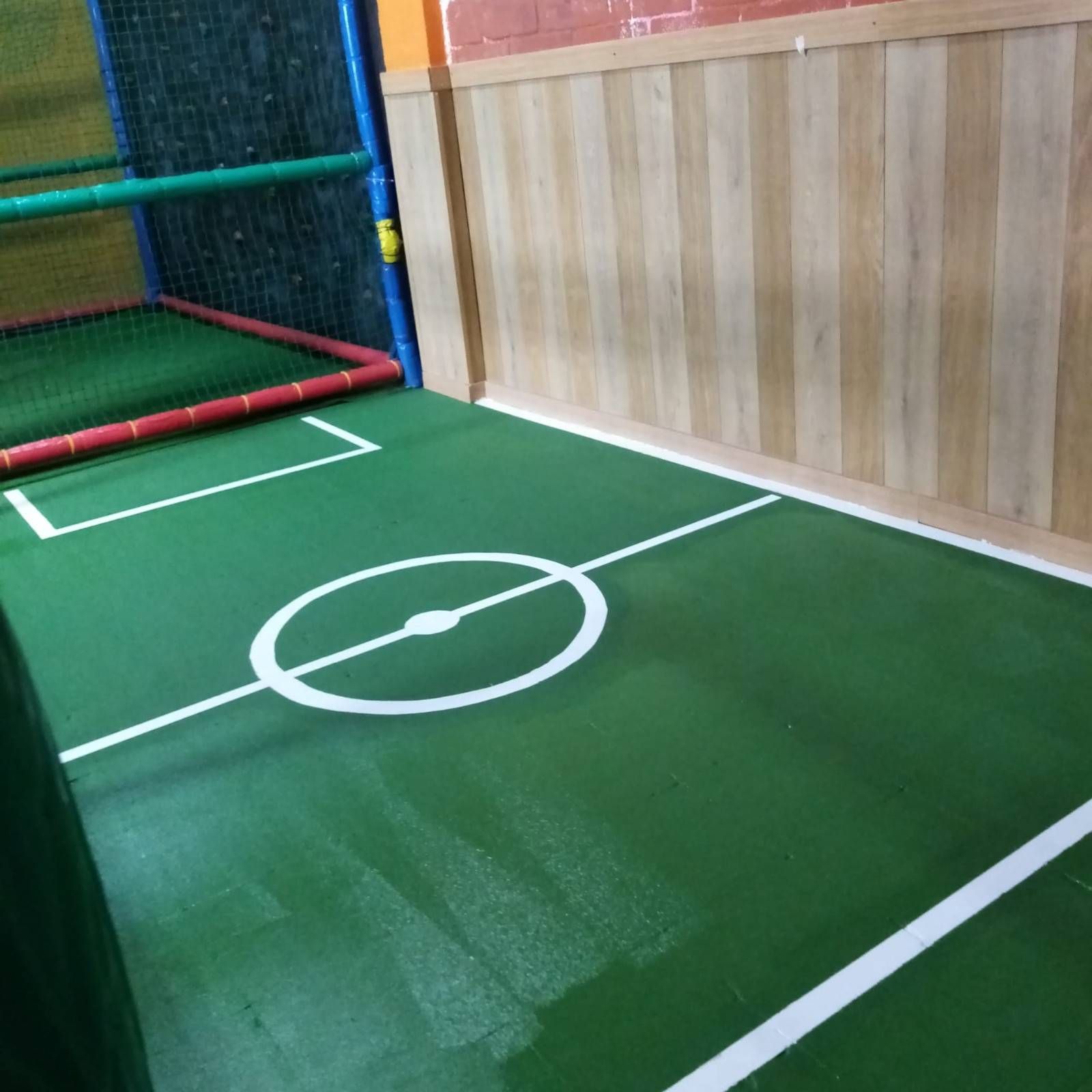 Cancha de minifútbol cubierta con césped verde, líneas blancas y una red de portería en la esquina.