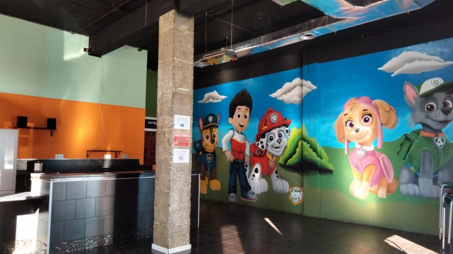 Mural interior de perros de dibujos animados en una pared junto a un mostrador negro y una zona de asientos naranja.