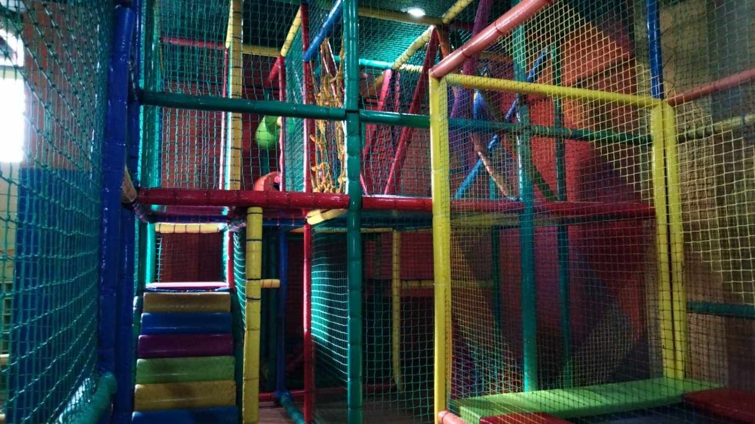 Parque infantil interior colorido con redes y plataformas para trepar de color rojo, amarillo y azul.