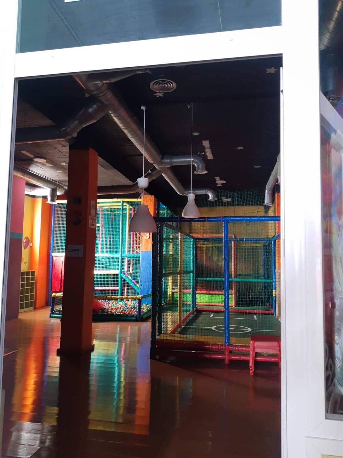 Zona de juegos interior colorida con estructuras acolchadas para trepar, cerramientos de malla.