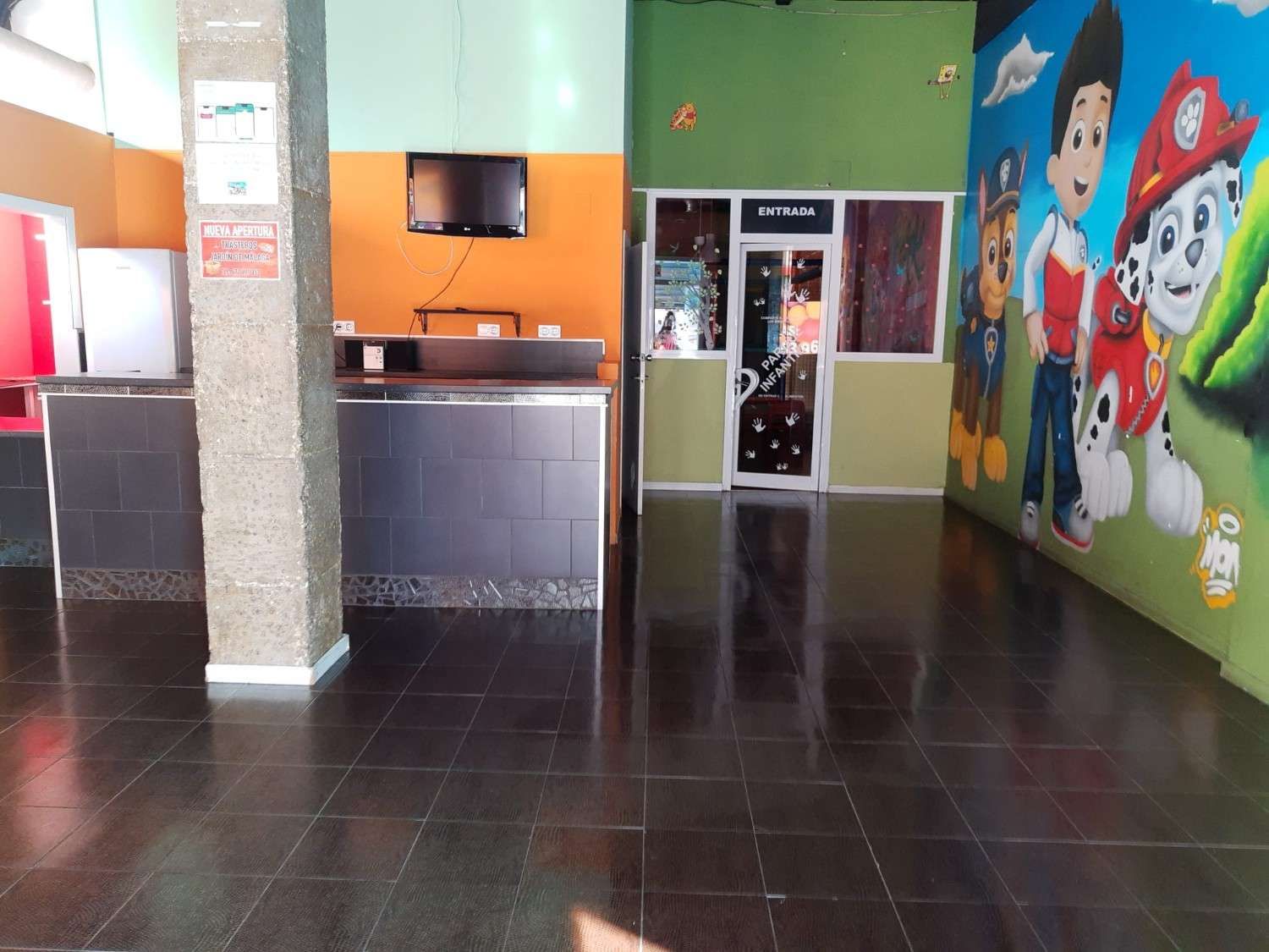 Vestíbulo luminoso con suelo de baldosas, mostrador de recepción y un colorido mural de dibujos animados en la pared derecha.