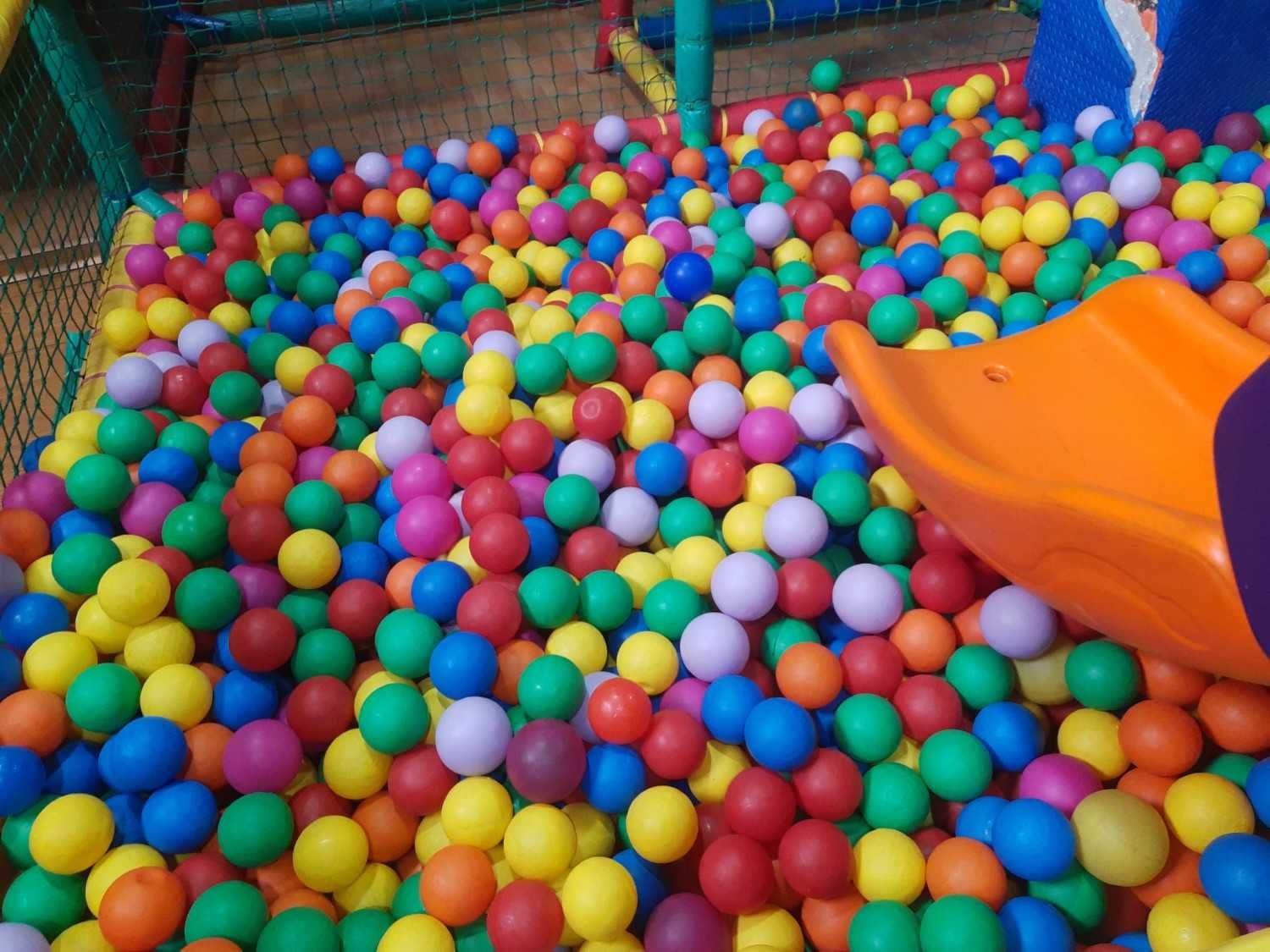 Piscina de bolas colorida con tobogán naranja en un área de juegos interior.