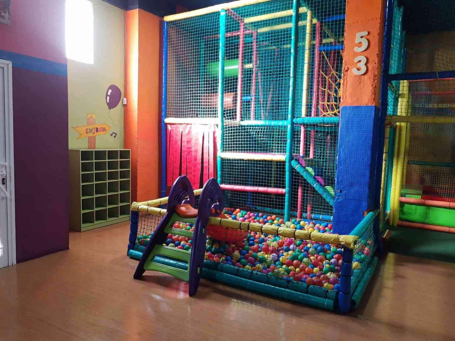 Zona de juegos infantil interior con colorida estructura de escalada con red y piscina de bolas.