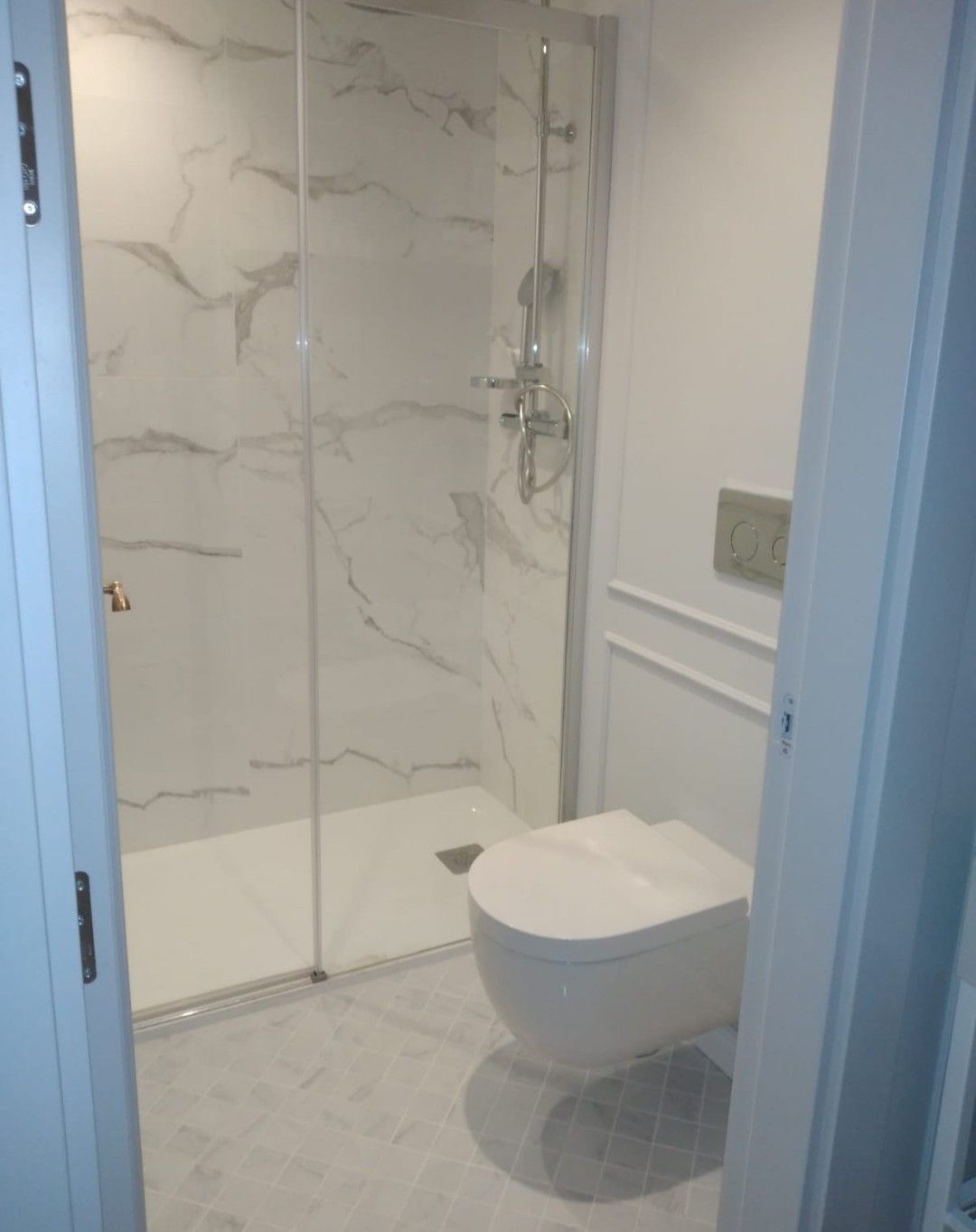 Baño pequeño y moderno con ducha de cristal e inodoro blanco suspendido.